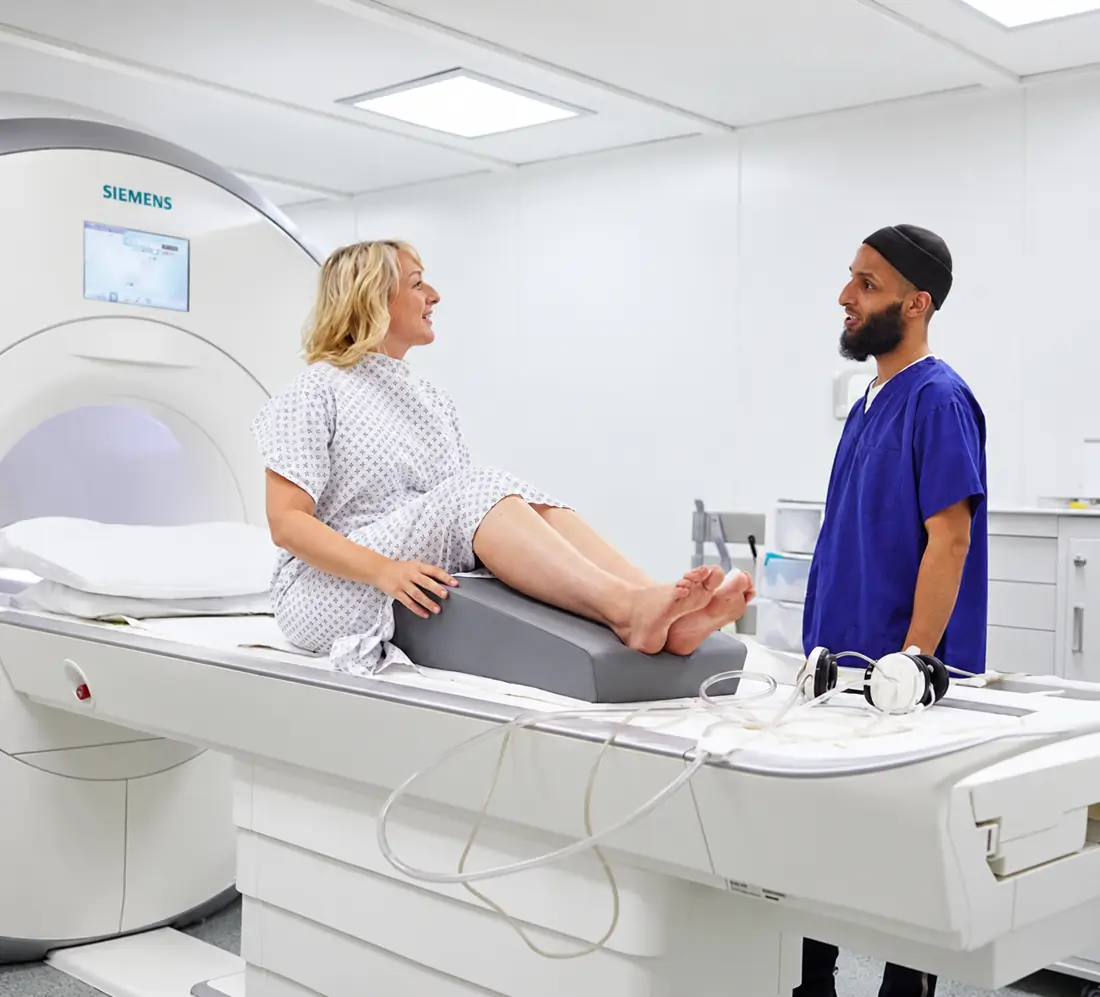 A radiographer talking with a patient on an MRI table, with her leg supported